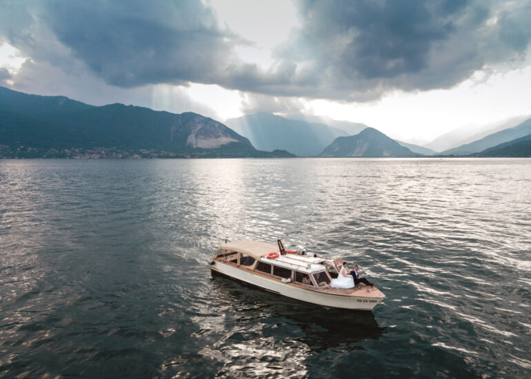 Lake Maggiore wedding photographer, drone shot with bride and groom on boat in the middle of Lake Maggiore and a stunning view of the lake and Alps